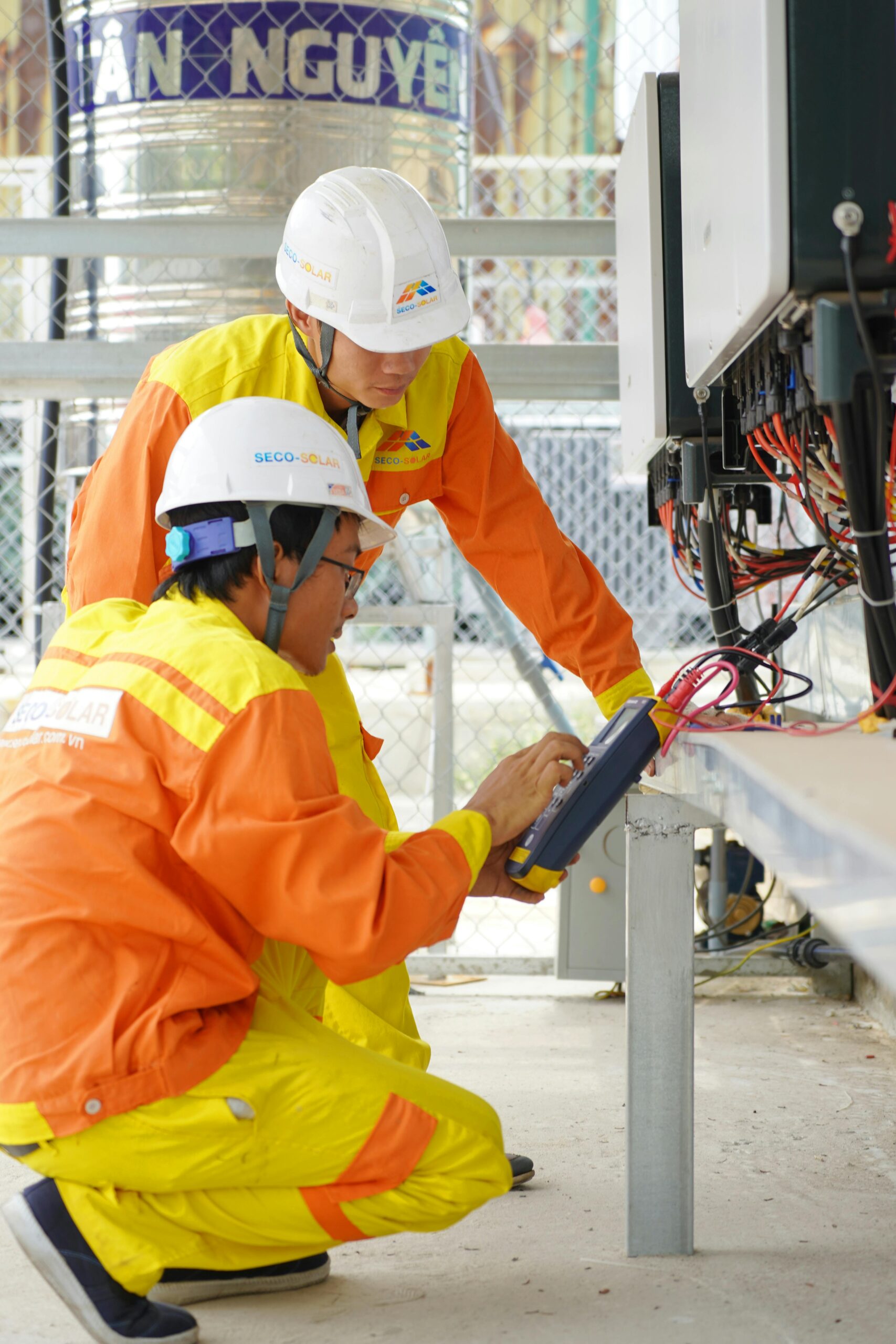 Two technicians in uniforms operating industrial machinery indoors, focused on technical maintenance.